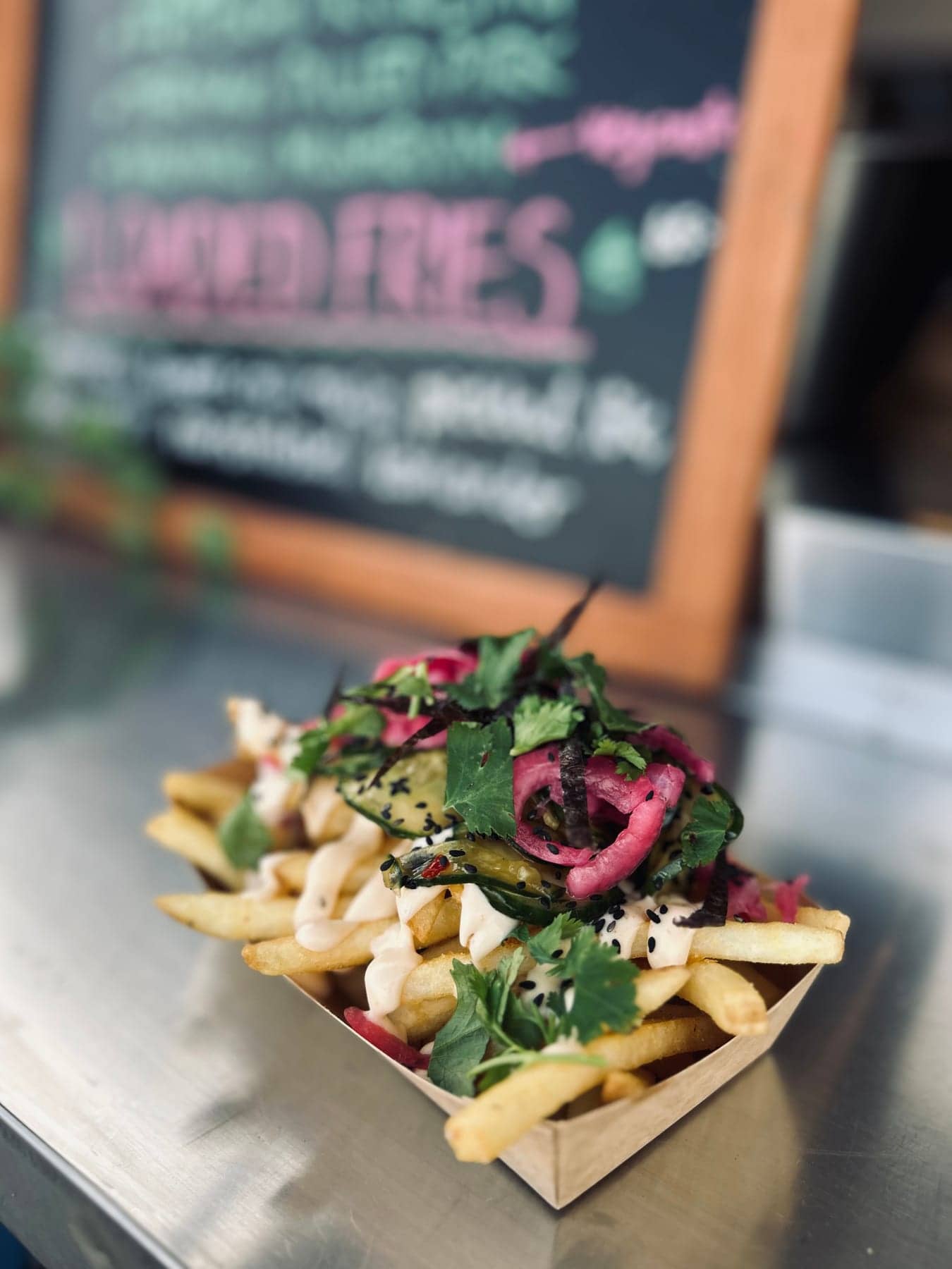 Pommes med topping och örter serverade framför foodtruckens menytavla