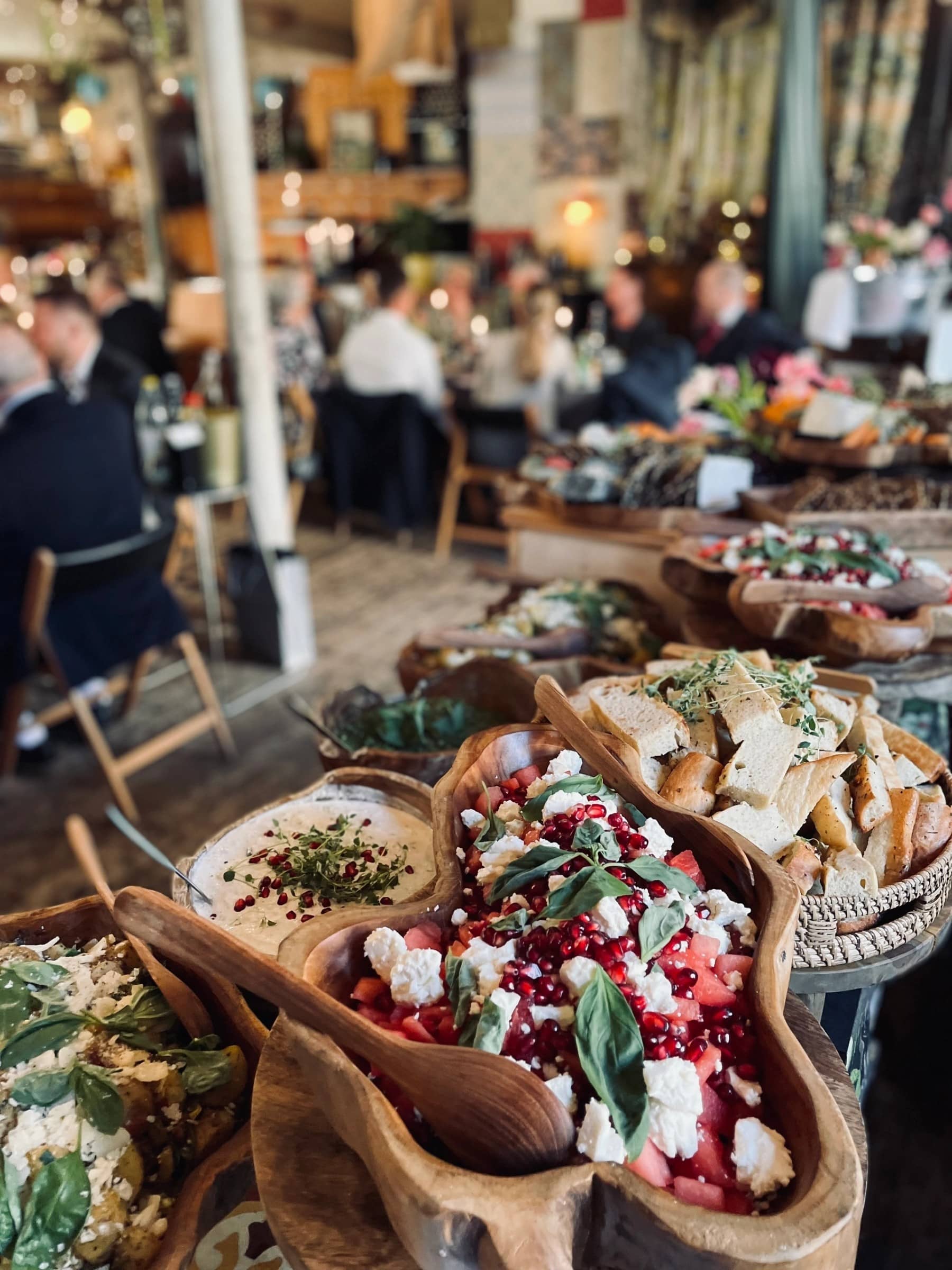 Buffébord med bröd, sallader och gäster i bakgrunden